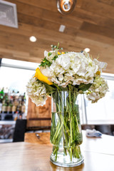 Closeup of one wedding flower bouquet arrangement on wooden table of reception dinner in restaurant venue, alcohol bar background