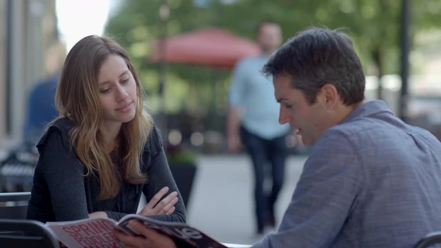 Beautiful female sits speaking to handsome male outside at restaurant