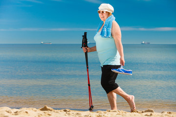 Senior woman practicing nordic walking on beach