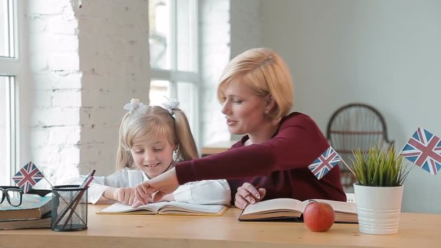 Highly professional english tutor helping the pupil to understand unknown words, having a lesson in comfortable light classroom, wearing dark cherry sweatshirt and pristine white blouse