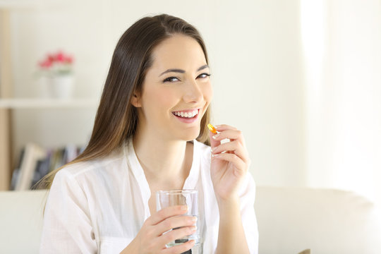 Happy woman taking a vitamin supplement pill looking at you