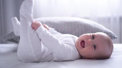 Funny chubby baby playing with feet on bed - Powered by Adobe
