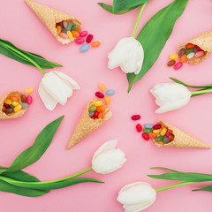 Composition with bright sugar candy in waffle cones and white flowers on pink background. Flat lay, top view