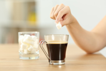 Woman hand throwing sugar cube into a coffee mug