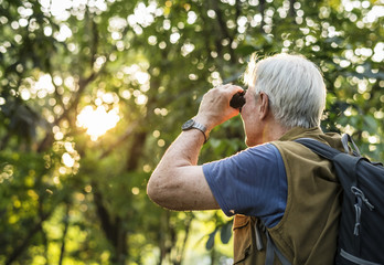 Elderly man watching birds with binoculars - obrazy, fototapety, plakaty