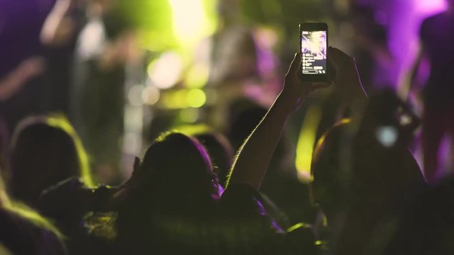 Hands in the crowd holding smart phone and shooting musical performance. Bright illumination on the stage