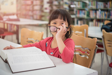 Cute little girl studying at the library and smiling