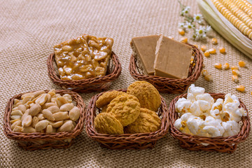 Group of food of Festa Junina in wicker baskets, typical brazilian party: Peanut, Cookie, Popcorn, Pe de Moleque, Pacoca, Corn. Jute fabric on table.