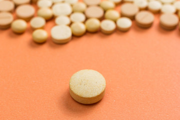 Heap of assorted beige capsules on orange table. One pill is apart, isolated.