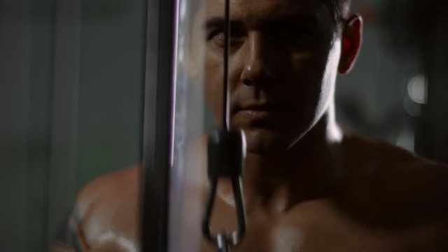 Closeup of muscular concentrated athlete with tattoo on arm doing rope triceps pushdowns in gym