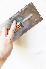 Woman hand with old metal spatula to equalize plaster filler on the wall