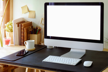 Loft workspace with blank screen desktop computer supplies on dark leather desk.