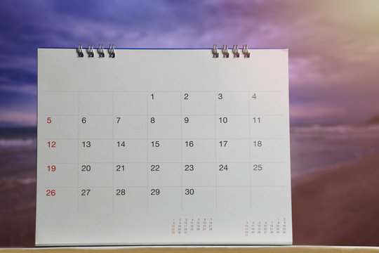 calendar is placed on a wooden floor on blur Beach in the evening background.