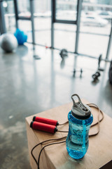 Naklejka premium closeup view of jump rope and bottle of water on wooden box at gym
