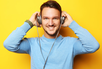 lifestyle and people concept: Happy young man listening to music with headphones over yellow background