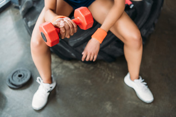 cropped image of sportswoman in wristbands doing exercise with dumbbell at gym