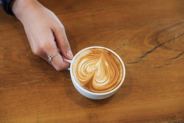 Female hands holding a cup of coffee with foam over wooden table, top view