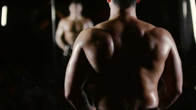 Rear view of athletic man with muscular back doing dumbbell lateral raise exercise while training in gym