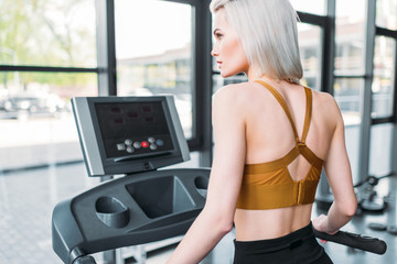 Fototapeta premium back view of young sportswoman training on treadmill at gym