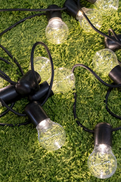 Closed Up Transparent Illuminated Lightbulb With Black Nylon Braided Cover Cord And Extension On Green Carpet Background