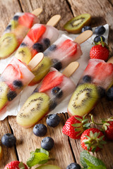 Freshly prepared popsicles ice with fresh strawberries, kiwi and blueberries on a stick close-up. vertical