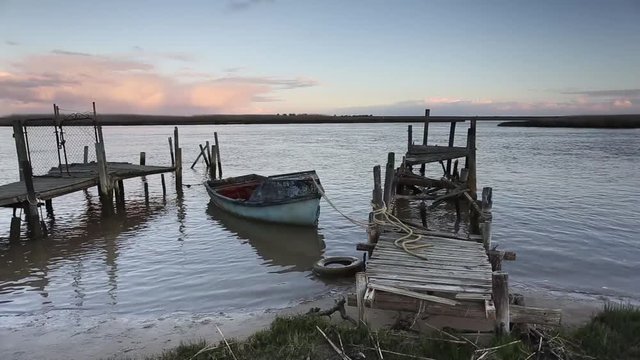 Realtime footage of a single row boat tied to a wooden dock on a lake at dusk