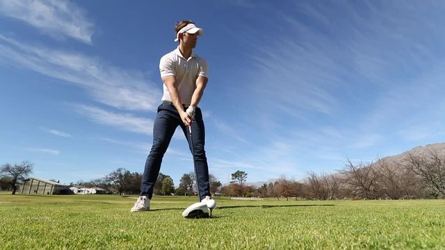 Wide low angle shot of a young male golfer swinging on a beautiful green golf course