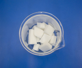 White chemical ingredient in clear beaker on blue table background for science lab experiment.