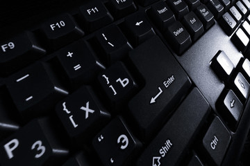 Black computer keyboard close-up in light of monitor.
