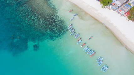 Aerial: Shoreline with thai fishing boats and long tail taxi boats parking along the sand beach of Thailand