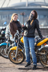 Fototapeta na wymiar Two women motorcyclists making photo with selfie stick and front camera of cellular