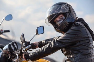 Motorcycle driver in black outfit holding steering wheel and looking at camera, Caucasian woman