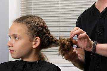 the hairdresser plaits a pigtail to the child, with curly hair