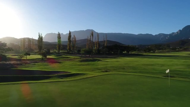 Aerial drone shot over a beautiful green golf course empty with trees and mountains in South Africa