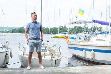 Obraz premium Attractive man stands at the nose of a boats on pier at river marina