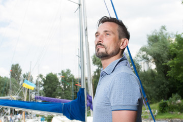 Successful young businessman is enjoying free time at the marina. Yachtsmen portrait with boat