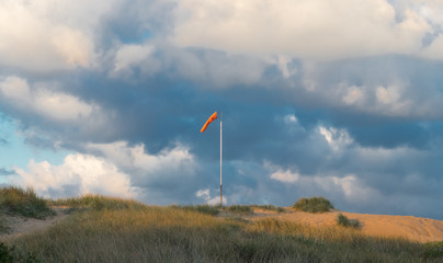 Windsock blowing on a sand dune with clouds in the background.