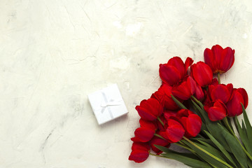 Red Tulips and White Gift Box on a Light Stone Background. Concept gifts and surprises from a loved one. Flat lay, top view