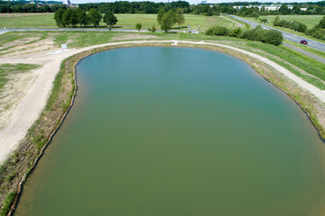 Rainwater retention basin with turquoise coloured water, taken diagonally from the air with a drone