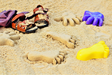 Fototapeta na wymiar Sand on the beach or in the sandbox and footprints in the sand. Form for sand and children's shoes nearby. Can be used as a background image to copy space.