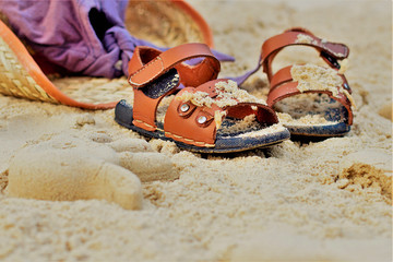 Fototapeta na wymiar Sand on the beach or in the sandbox and footprints in the sand. Form for sand and children's shoes nearby. Nearby accessories to protect the sun rays of parents. Background image for copy space.