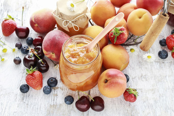 Jar of peach jam and summer fruits around.