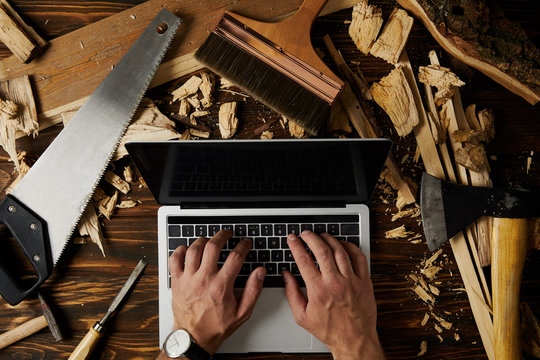 cropped image of carpenter typing on laptop surrounded by different tools on table