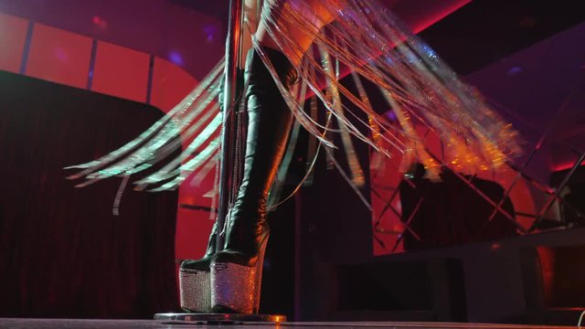 Sexy woman in high boots on platform and heel with rhinestones. Fringe skirt with pendants made of shiny stones. striptease dancer moving on stage in strip night club,