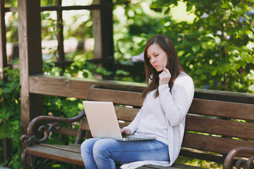 Young successful businesswoman in light casual clothes. Woman sitting on bench working on modern laptop pc computer in city park in street outdoors on nature. Mobile Office. Freelance business concept