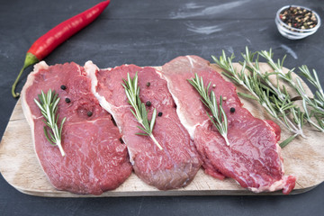Raw pork steak with black pepper peas and rosemary close-up on a dark background