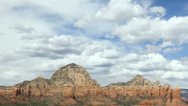 This looping video footage features clouds floating, in faster time lapse fashion, over the rugged and rocky peaks and summits surrounding Sedona, Arizona.