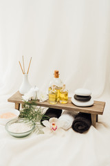 close up view of arrangement of spa treatment accessories with orchid flower, towels, oil and salt on white background