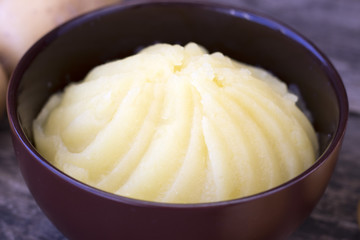 Mashed potatoes and raw potatoes side by side, located on a wooden background, rustic style close-up