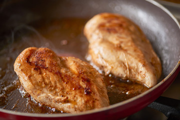 Two chicken breast pieces frying in a pan